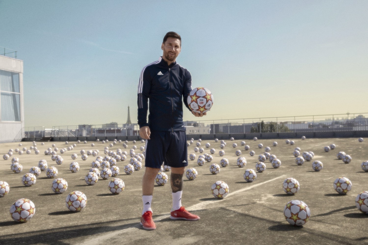 Lionel Messi, un ballon à la main, debout sur un toit au milieu de centaines de ballons, Paris à l'horizon