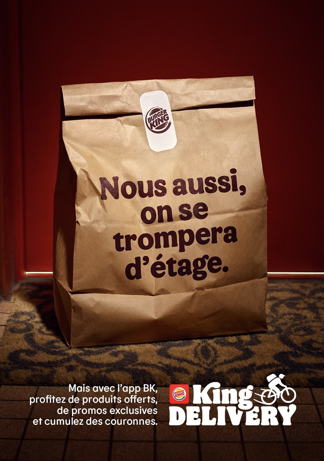 Affiche « Nous aussi, on se trompera d'étage. » : sac Burger King posé sur un paillasson